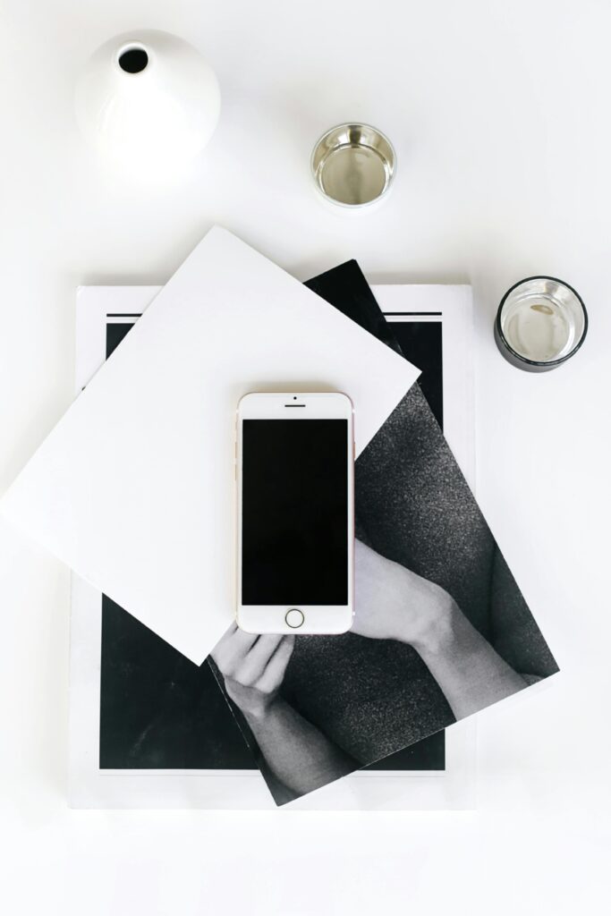 A flat lay photo of a minimalist workspace featuring a smartphone, books, and a vase.