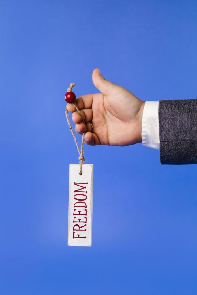 Close-up of a hand holding a 'Freedom' tag on a blue background.